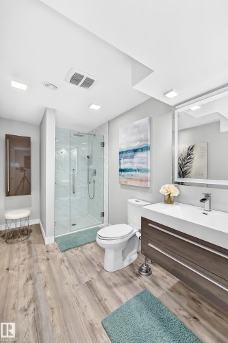 Bathroom featuring a glass-enclosed shower with tiled walls, wood-finish flooring, a contemporary vanity with an integrated sink, a wall-mounted mirror, and recessed lighting - 823 77 Street Sw, Edmonton, AB - Indoor Photo Showing Bathroom