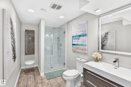 Contemporary full bathroom featuring a glass-enclosed shower with tile surround, wood-finish flooring, a floating vanity with integrated sink, and an illuminated mirror - 823 77 Street Sw, Edmonton, AB - Indoor Photo Showing Bathroom