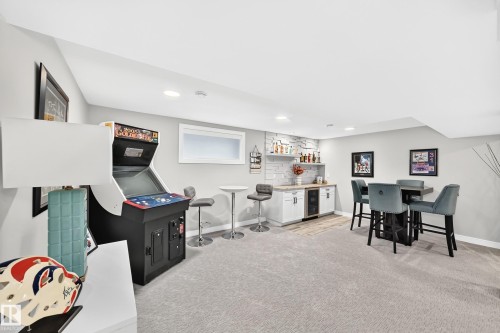 Finished basement featuring light gray carpeting, a built-in wet bar with white cabinetry, a beverage refrigerator, and stone-look accent wall - 823 77 Street Sw, Edmonton, AB - Indoor