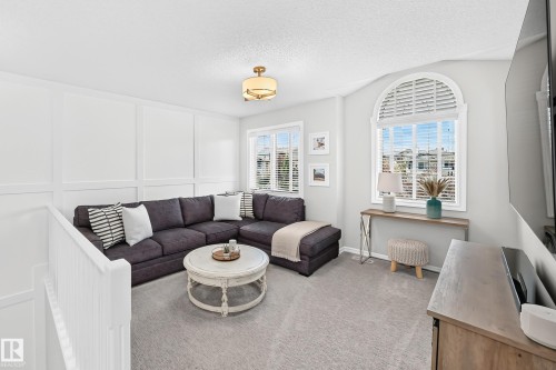 Carpeted recreational space featuring wainscoting, an arched window with louvered blinds, and a built-in entertainment console - 823 77 Street Sw, Edmonton, AB - Indoor Photo Showing Living Room