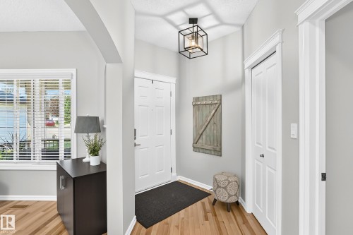 Welcoming entry featuring light wood-finish flooring, a white paneled entry door, a contemporary black geometric flush-mount light fixture, and a white trim package - 823 77 Street Sw, Edmonton, AB - Indoor Photo Showing Other Room