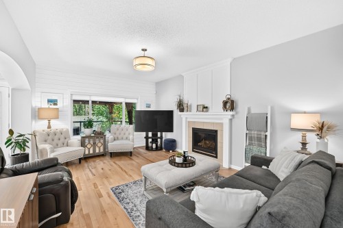 Living area featuring wood-finish flooring, a fireplace with a tile surround and white mantel, and a sliding glass door - 823 77 Street Sw, Edmonton, AB - Indoor Photo Showing Living Room With Fireplace