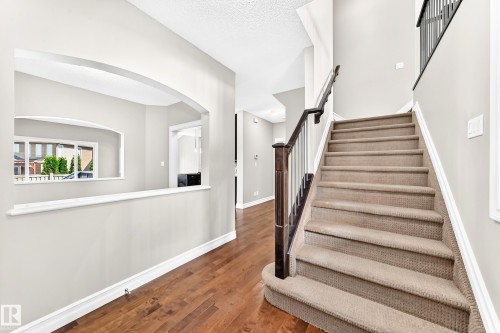 Wood-finish flooring, staircase with carpeted treads, dark wood newel posts and handrail, and an arched wall opening - 4212 Charles Close Sw, Edmonton, AB - Indoor Photo Showing Other Room