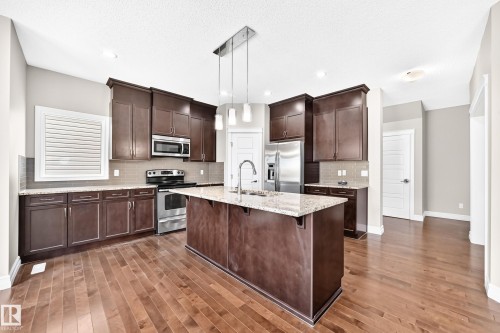 Kitchen featuring wood-finish flooring, dark wood cabinetry, stainless steel appliances, a center island with a sink, and pendant lighting - 4212 Charles Close Sw, Edmonton, AB - Indoor Photo Showing Kitchen With Stainless Steel Kitchen With Upgraded Kitchen