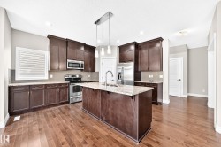 Kitchen featuring wood-finish flooring, dark wood cabinetry, stainless steel appliances, a center island with a sink, and pendant lighting - 