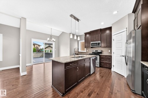 Kitchen featuring wood-finish flooring, dark wood cabinetry, stainless steel appliances, and a central island with a light-colored countertop - 4212 Charles Close Sw, Edmonton, AB - Indoor Photo Showing Kitchen With Stainless Steel Kitchen With Double Sink With Upgraded Kitchen