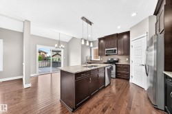Kitchen featuring wood-finish flooring, dark wood cabinetry, stainless steel appliances, and a central island with a light-colored countertop - 