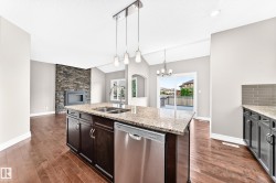 Spacious kitchen island with granite countertop and stainless steel appliances, wood-finish flooring, stone-clad fireplace, vaulted ceiling, and sliding glass doors to outdoor deck space - 