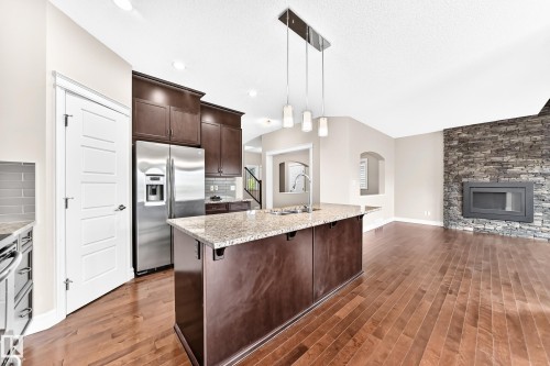 Kitchen island with a light-toned countertop, stainless steel refrigerator, dark wood-finish cabinetry, and wood-finish flooring - 4212 Charles Close Sw, Edmonton, AB - Indoor Photo Showing Kitchen With Stainless Steel Kitchen With Upgraded Kitchen