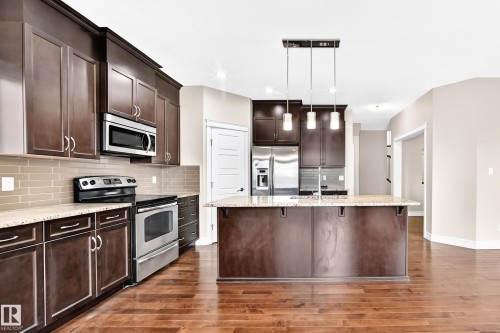 Dark wood-finish cabinetry, stainless steel appliances, light-toned granite-style countertops, wood-finish flooring, and a kitchen island with pendant lighting - 4212 Charles Close Sw, Edmonton, AB - Indoor Photo Showing Kitchen With Upgraded Kitchen
