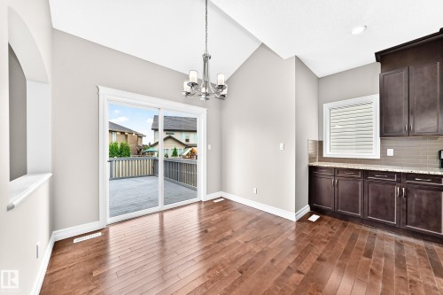 Vaulted ceiling with a chandelier, wood-finish flooring, dark wood cabinetry, light-colored countertops, and glass sliding doors leading to a wood deck - 4212 Charles Close Sw, Edmonton, AB - Indoor Photo Showing Kitchen