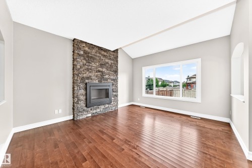 Stone-clad fireplace with an integrated firebox, rich wood-finish flooring, and vaulted ceilings - 4212 Charles Close Sw, Edmonton, AB - Indoor Photo Showing Living Room With Fireplace
