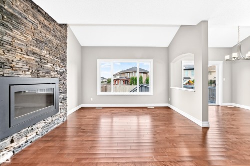 Stacked stone fireplace with a black metal insert, wide plank wood-finish flooring, and white trim - 4212 Charles Close Sw, Edmonton, AB - Indoor Photo Showing Living Room With Fireplace