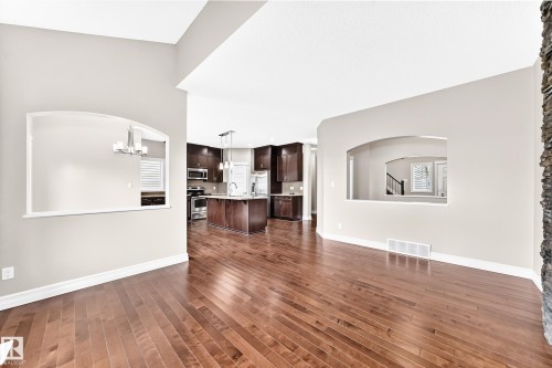Hardwood flooring, arched wall cut-outs, high ceilings, dark wood-finish cabinetry, and a stacked stone-finish accent wall - 4212 Charles Close Sw, Edmonton, AB - Indoor Photo Showing Other Room