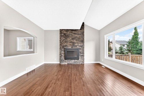 Vaulted ceiling with wood-finish flooring, featuring a stacked stone fireplace, large windows, and a decorative interior archway - 4212 Charles Close Sw, Edmonton, AB - Indoor Photo Showing Living Room With Fireplace