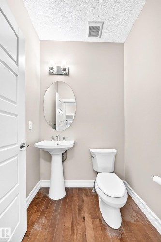 Wood-finish flooring, pedestal sink with chrome faucet, oval wall mirror, and two-light vanity fixture - 4212 Charles Close Sw, Edmonton, AB - Indoor Photo Showing Bathroom