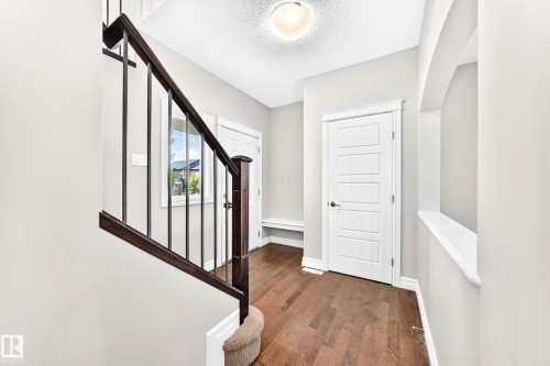 Hardwood flooring, dark wood newel post and handrail, wrought iron balusters, white trim, and a contemporary five-panel door - 4212 Charles Close Sw, Edmonton, AB - Indoor Photo Showing Other Room