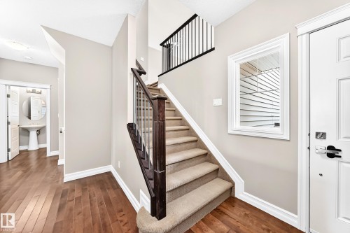 Wood-finish flooring, staircase with carpeted treads, dark wood newel post, metal balusters, and a white paneled door - 4212 Charles Close Sw, Edmonton, AB - Indoor Photo Showing Other Room