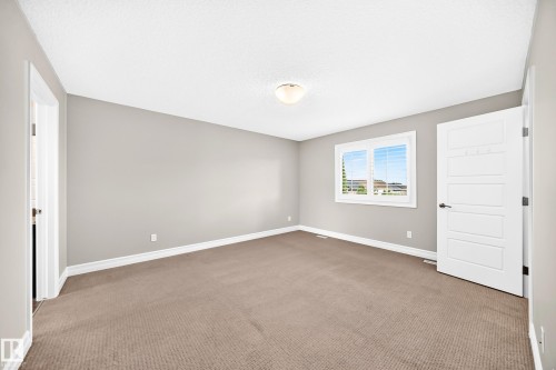 Neutral-toned walls, textured carpet flooring, window with horizontal blinds, and a white interior door with black hardware - 4212 Charles Close Sw, Edmonton, AB - Indoor Photo Showing Other Room