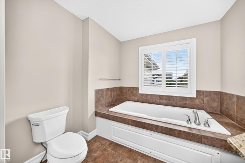 Built-in soaking tub with chrome fixtures, surrounded by brown tile and a granite-finish countertop - 4212 Charles Close Sw, Edmonton, AB - Indoor Photo Showing Bathroom