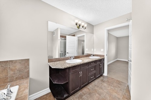 Dual vanity with granite-finish countertop, undermount sinks, and dark wood-finish cabinetry - 4212 Charles Close Sw, Edmonton, AB - Indoor Photo Showing Bathroom