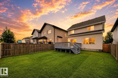 Expansive green lawn with a wood fence, featuring a raised deck with stairs and a two-story home with siding - 4212 Charles Close Sw, Edmonton, AB - Outdoor