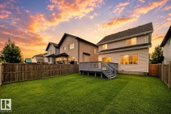 Expansive green lawn with a wood fence, featuring a raised deck with stairs and a two-story home with siding - 