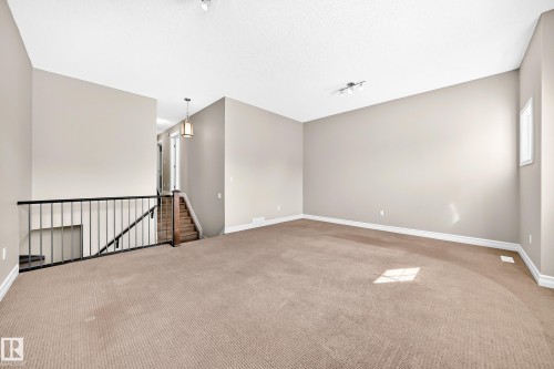 Open-concept area featuring light-toned carpeting, neutral wall paint, and a black metal railing - 4212 Charles Close Sw, Edmonton, AB - Indoor Photo Showing Other Room