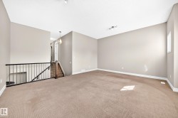 Open-concept area featuring light-toned carpeting, neutral wall paint, and a black metal railing - 