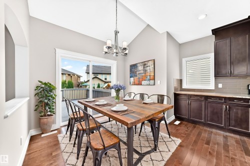 Vaulted ceiling, wood-finish flooring, sliding glass door, built-in cabinetry, and a contemporary chandelier - 4212 Charles Close Sw, Edmonton, AB - Indoor Photo Showing Dining Room