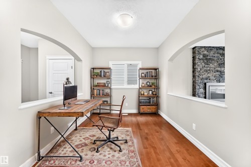 Hardwood flooring with a stone-clad fireplace visible through an arched opening - 4212 Charles Close Sw, Edmonton, AB - Indoor Photo Showing Office