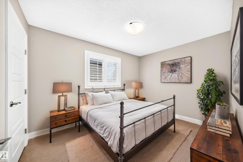 Serene primary bedroom showcasing a metal-frame bed, warm wood-finish nightstands with integrated lighting, neutral wall finishes, and abundant natural light from shuttered windows - 4212 Charles Close Sw, Edmonton, AB - Indoor Photo Showing Bedroom