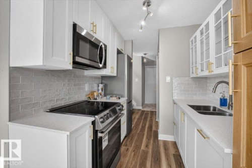 Contemporary kitchen featuring white cabinetry, stainless steel appliances, wood-finish flooring, and light-toned countertops - #205 11429 124 St Nw, Edmonton, AB - Indoor Photo Showing Kitchen With Double Sink With Upgraded Kitchen