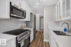 White cabinetry with gold-tone hardware, stainless steel appliances, light-toned countertops, subway tile backsplash, and wood-finish flooring - 