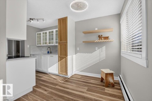 Kitchen and dining area featuring wood-finish flooring, white cabinetry with glass inserts, a white subway tile backsplash, and two wall-mounted floating shelves - #205 11429 124 St Nw, Edmonton, AB - Indoor Photo Showing Other Room