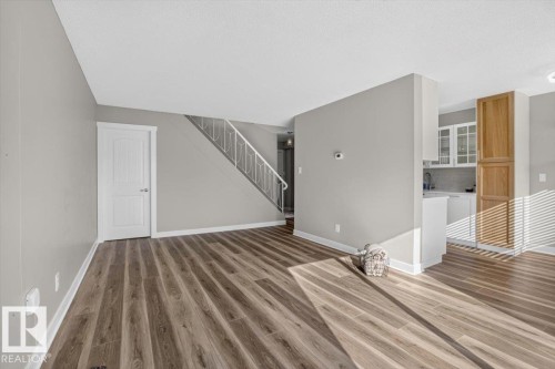 Wood-finish flooring, staircase with white railing, light gray wall finishes, white doors, and built-in kitchen cabinetry - #205 11429 124 St Nw, Edmonton, AB - Indoor Photo Showing Other Room