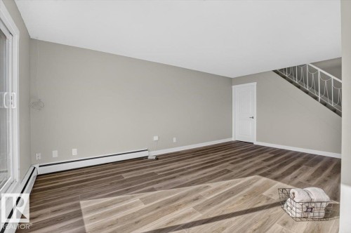 Wood-finish flooring, light gray wall color, white trim, sliding glass door, and a staircase with white railing - #205 11429 124 St Nw, Edmonton, AB - Indoor Photo Showing Other Room