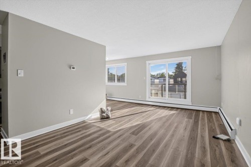 Wood-finish flooring throughout, light gray wall paint, and white trim - #205 11429 124 St Nw, Edmonton, AB - Indoor Photo Showing Other Room