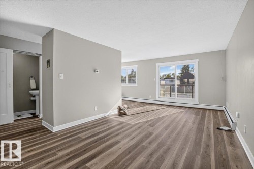 Spacious interior featuring wood-finish flooring, light grey wall paint, and white trim - #205 11429 124 St Nw, Edmonton, AB - Indoor
