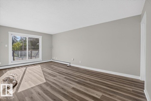 Spacious room with wood-finish flooring, light grey painted walls, and a large sliding glass door - #205 11429 124 St Nw, Edmonton, AB - Indoor