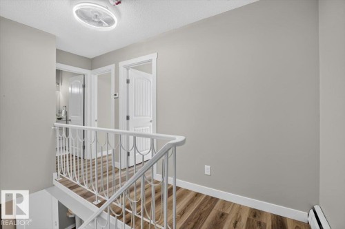 Light-toned walls, wood-finish flooring, white railing, and flush-mount ceiling light fixture - #205 11429 124 St Nw, Edmonton, AB - Indoor Photo Showing Other Room