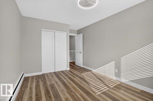 Wood-finish flooring, neutral gray walls, white trim, and a ceiling light fixture - #205 11429 124 St Nw, Edmonton, AB - Indoor Photo Showing Other Room