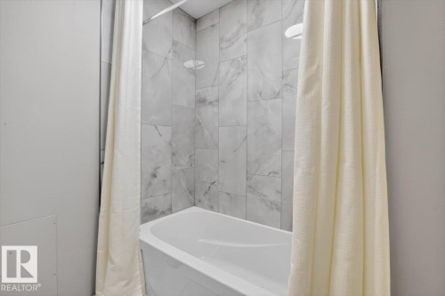 Bathtub with a white finish, light-toned wall tiling, and a ceiling-mounted showerhead - #205 11429 124 St Nw, Edmonton, AB - Indoor Photo Showing Bathroom
