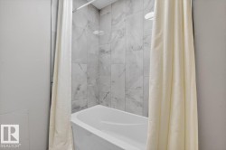 Bathtub with a white finish, light-toned wall tiling, and a ceiling-mounted showerhead - 