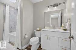 Bathroom featuring a built-in bathtub with tiled surround, wood-finish flooring, a white vanity with gold-tone hardware, and a rectangular mirror with track lighting - 