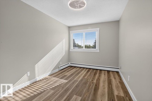 Light gray painted walls, wood-finish flooring, and a single window with white trim - #205 11429 124 St Nw, Edmonton, AB - Indoor Photo Showing Other Room
