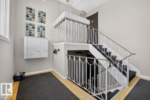 Multilevel staircase with white decorative railing, carpeted treads, and wood-finish flooring - #205 11429 124 St Nw, Edmonton, AB - Indoor Photo Showing Other Room