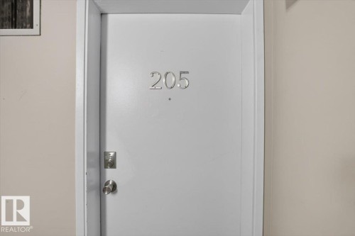 White entry door with a circular knob, deadbolt, and silver numerical address - #205 11429 124 St Nw, Edmonton, AB - 