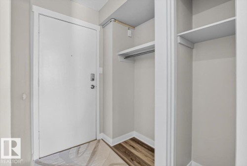 Entryway featuring a white door with contemporary hardware, wood-finish flooring, and a built-in closet with shelving and a hanging rod - #205 11429 124 St Nw, Edmonton, AB - Indoor