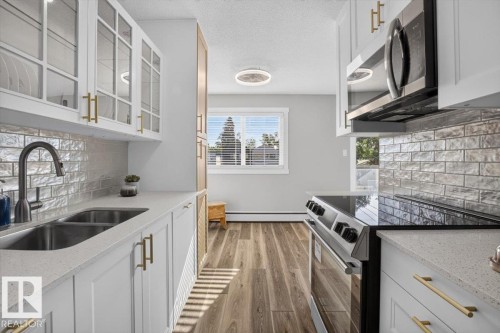 Modern kitchen with wood-finish flooring, white cabinetry, integrated stainless steel appliances, and a tile backsplash - #205 11429 124 St Nw, Edmonton, AB - Indoor Photo Showing Kitchen With Double Sink With Upgraded Kitchen